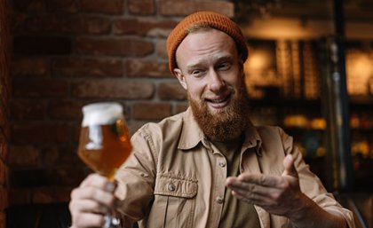 Man holding glass of beer at a distance, smiling at it. Adobe stock